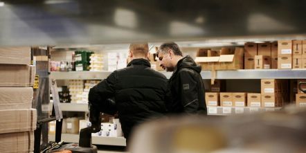 Divi darbinieki noliktavā pārbauda preču krājumus un apspriež darba uzdevumus